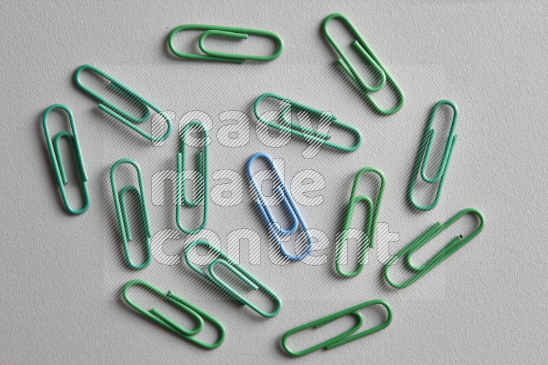 A bunch of green paper clips with a different colored paper clip in the center on grey background