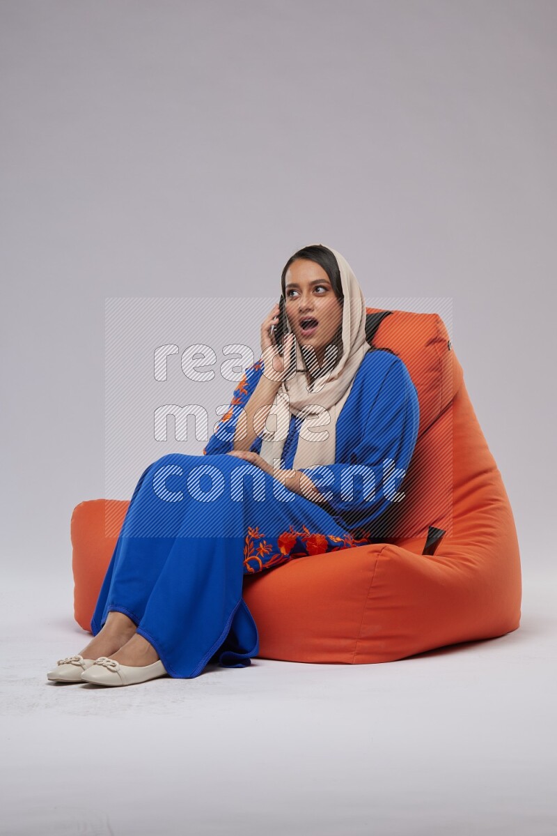A Saudi woman wearing Jalabiya sitting on an orange beanbag and talking on the phone