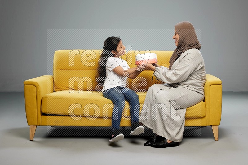 A girl sitting giving a cake to her mother on gray background
