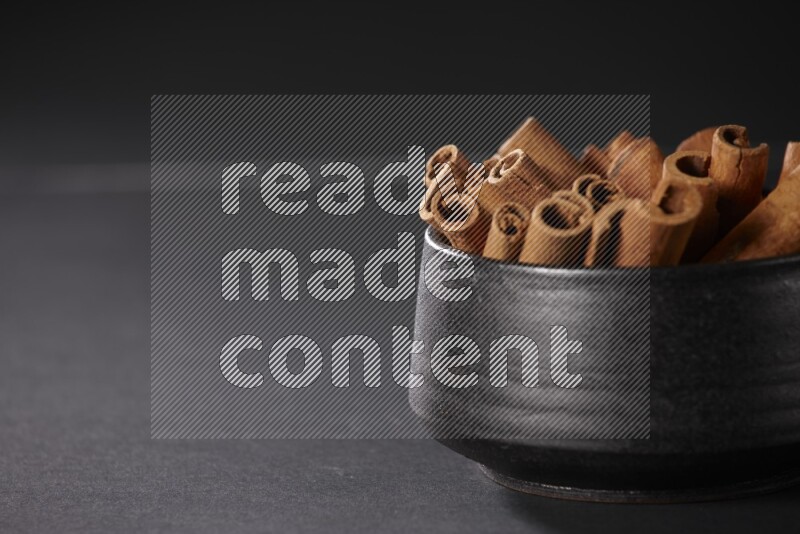 Cinnamon sticks in a black bowl on a black background in different angles