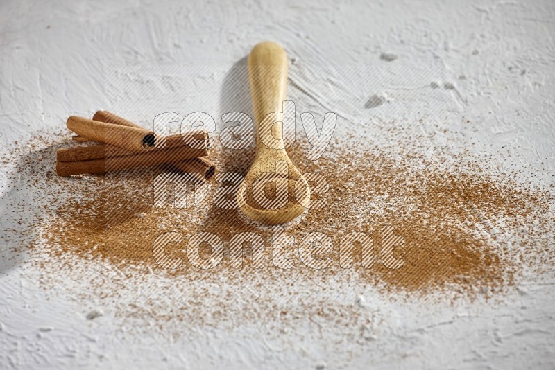 Cinnamon powder in a wooden spoon with cinnamon sticks and sprinkles powder on the flooring on white background