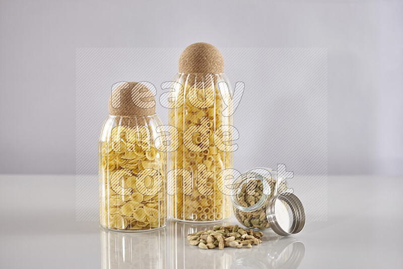 Raw pasta in glass jars with cardamom on light grey background