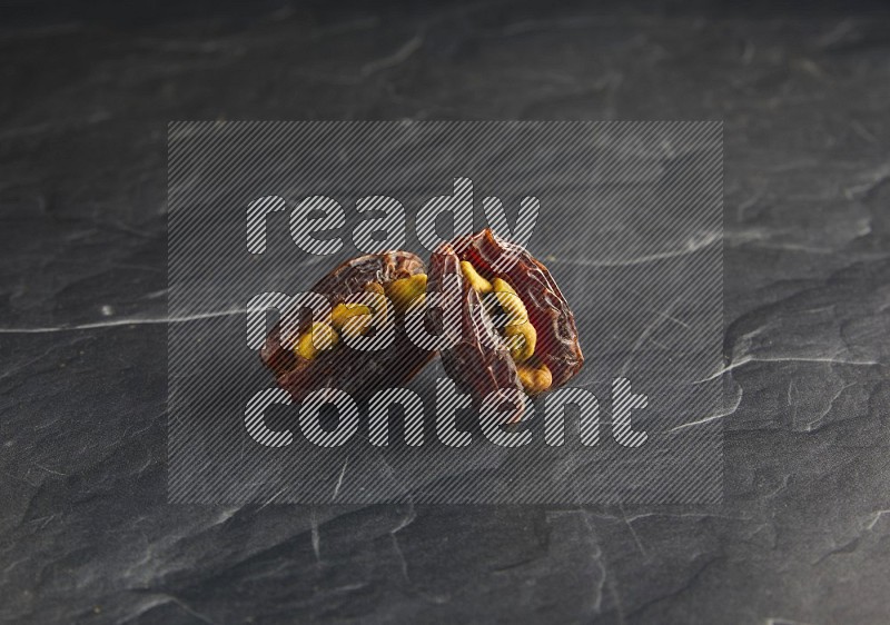 two pistachios stuffed madjoul dates on a black textured background