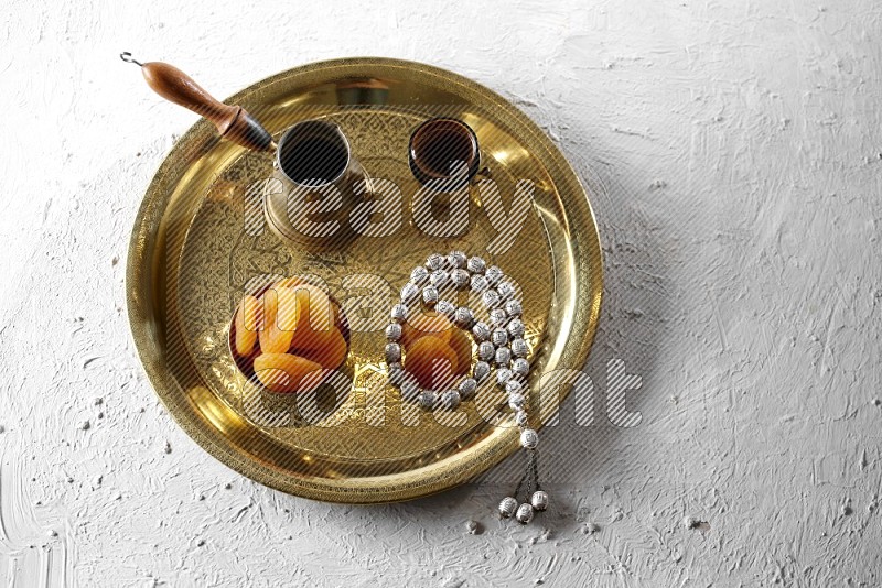 Dried apricots in a metal bowl with coffee and prayer beads on a tray in a light setup