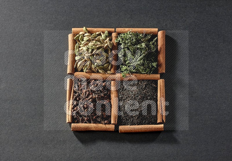 4 مربعات من عيدان القرفة ممتلئة بالشاي الأسود والقرنفل والنعناع المجفف وحبوب الهيل على أرضية سوداء
