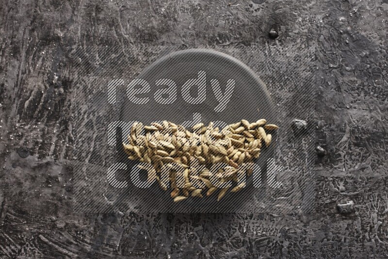 Cardamom on a black plate on textured black background