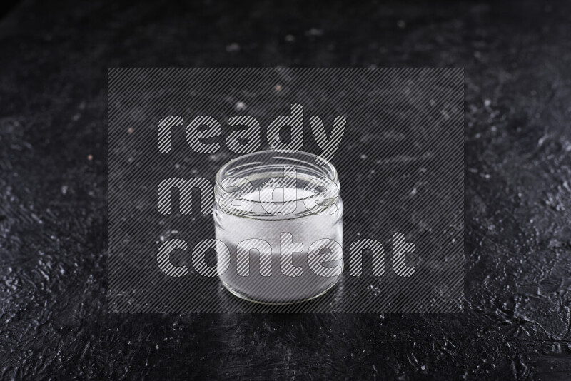 A glass jar full of fine table salt on black background