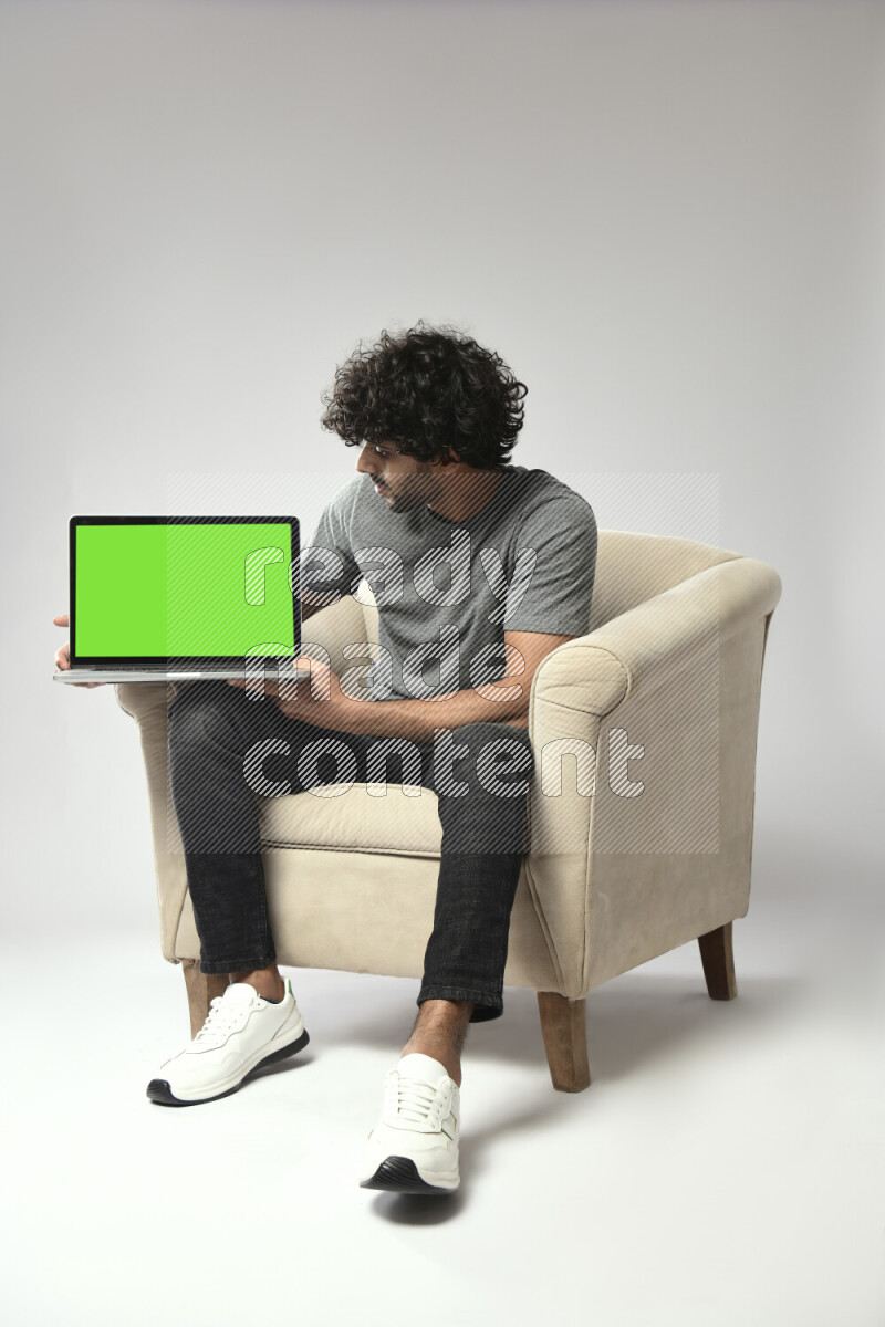 A man wearing casual sitting on a chair showing a laptop screen on white background
