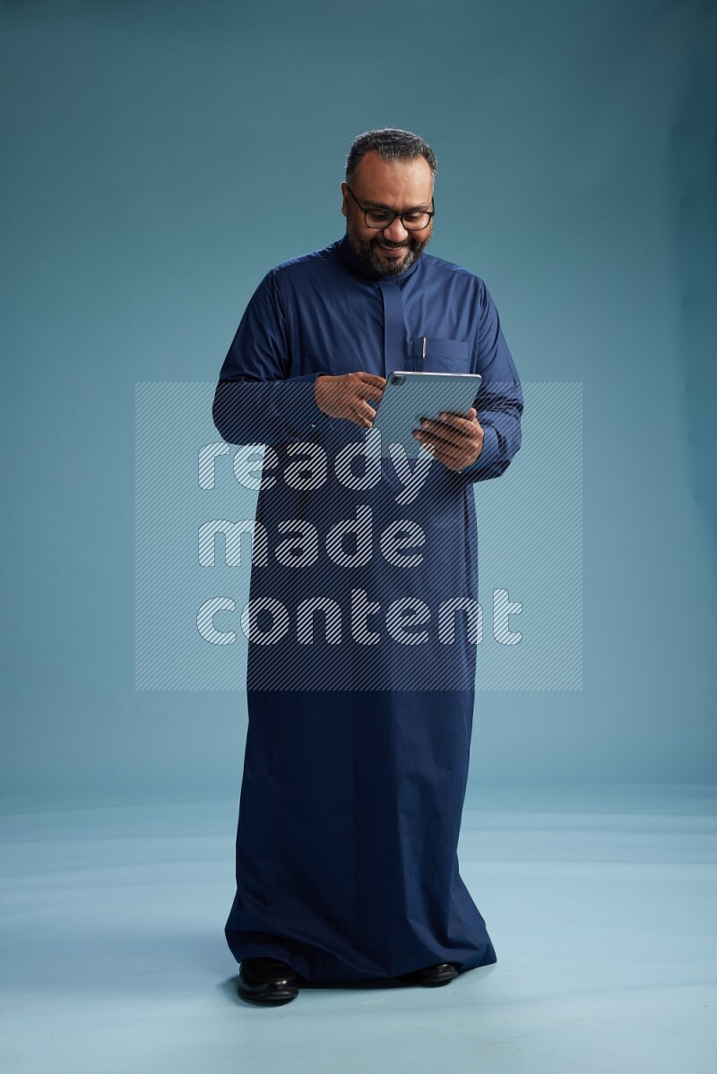 Saudi Man without shimag Standing working on tablet on blue background