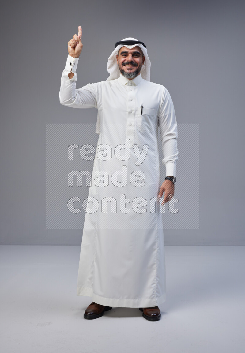 Saudi man Wearing Thob and white Shomag standing interacting with the camera on Gray background