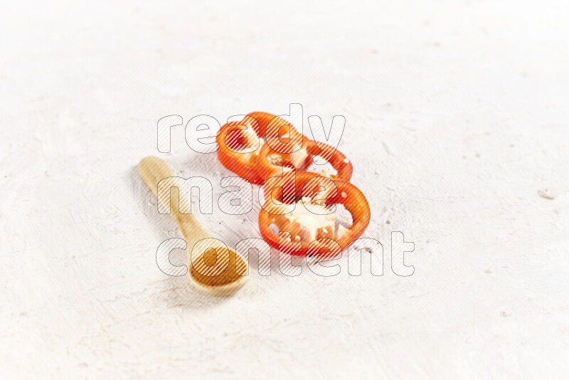 A wooden spoon full of ground paprika powder with red bell pepper slices beside it on white background