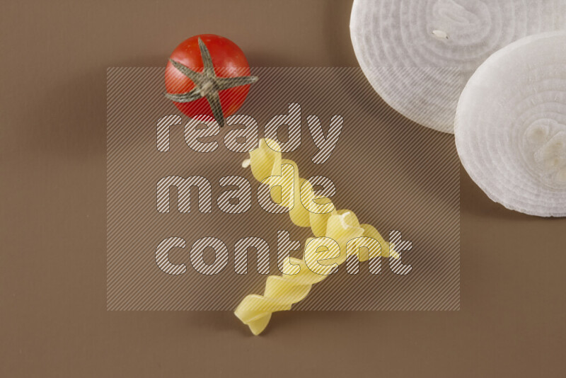 Raw pasta with different ingredients such as cherry tomatoes, garlic, onions, red chilis, black pepper, white pepper, bay laurel leaves, rosemary and cardamom on beige background