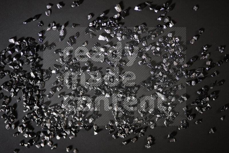 Black shimmering fragments of glass scattered on a black background