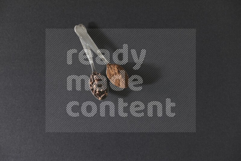 2 metal spoons, one full of cloves grains and the other full of cloves powder on a black flooring