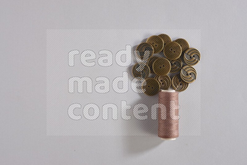 A brown sewing thread spool with colored buttons on grey background