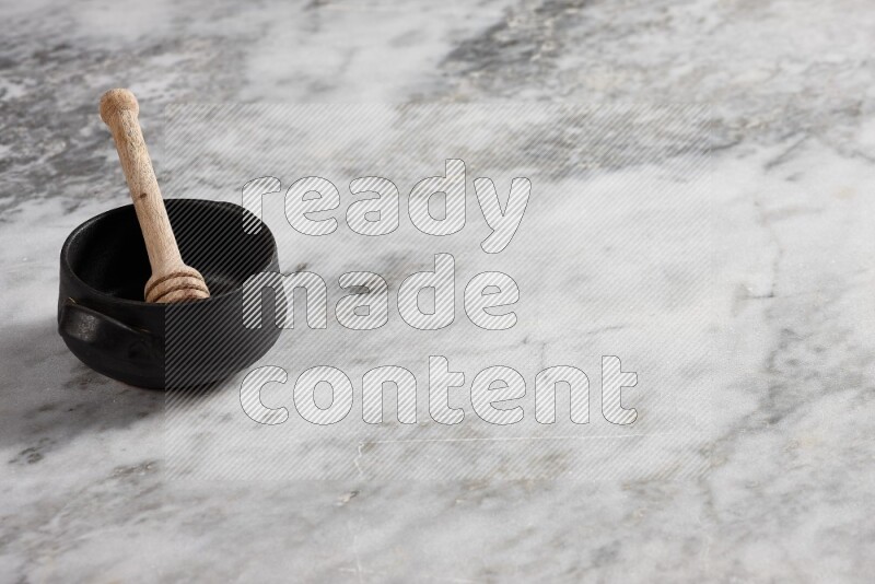 Black pottery bowl with wooden honey dipper in it on grey marble background