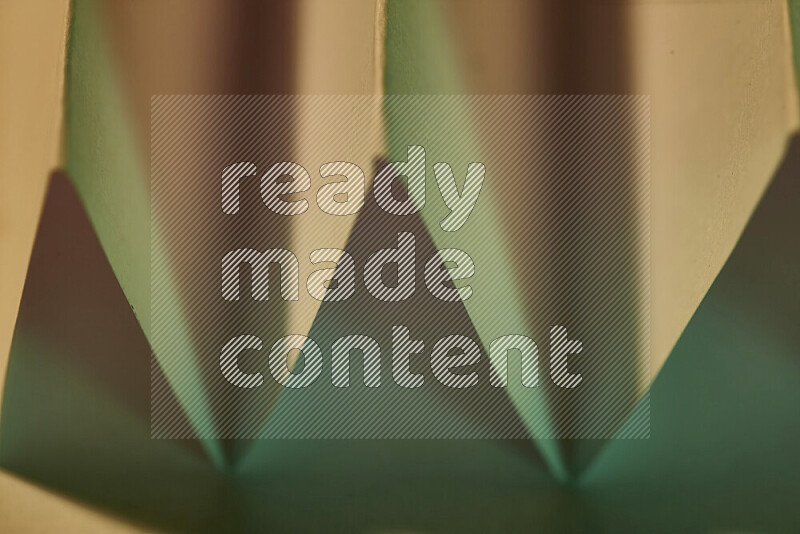 A close-up abstract image showing sharp geometric paper folds in green gradients and warm tones