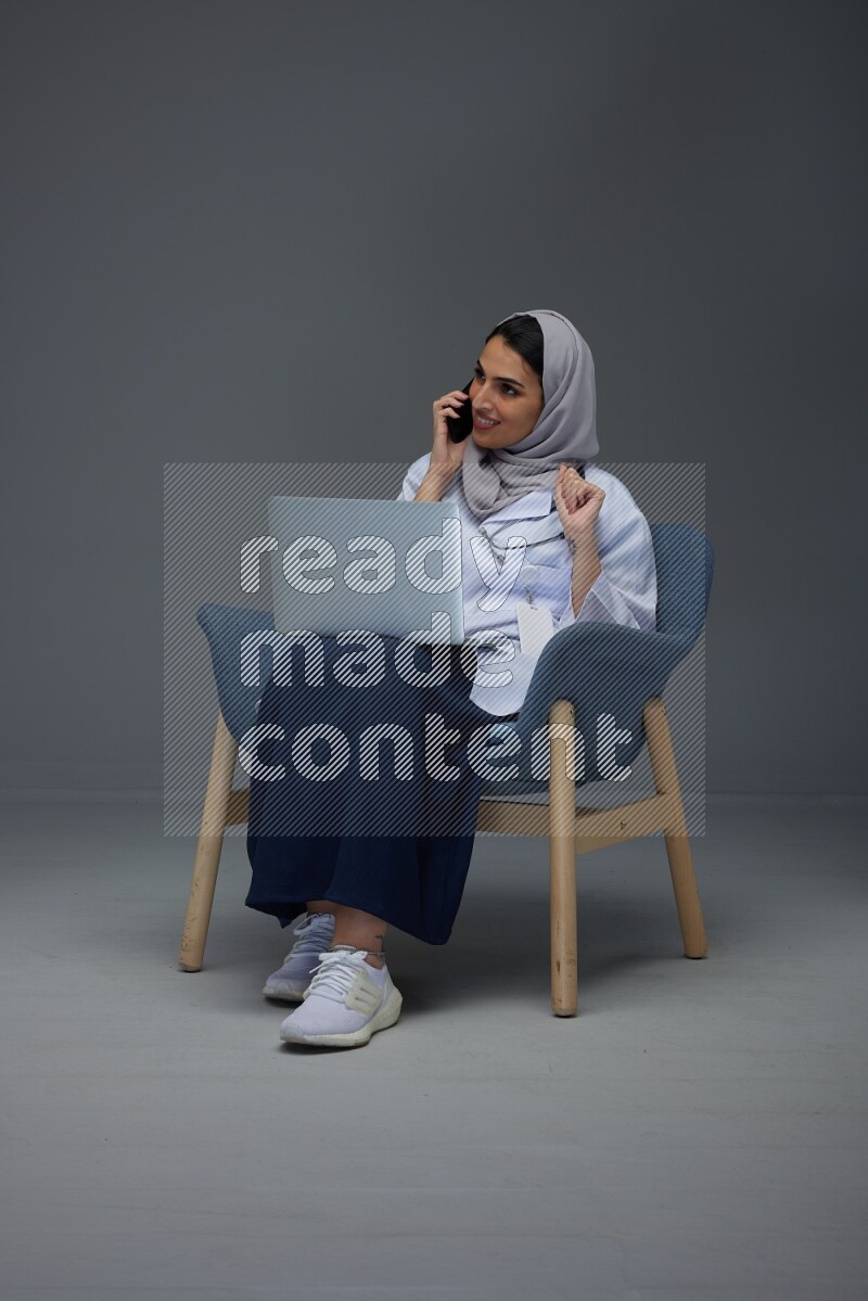 A doctor wearing a light gray head scarf sitting on blue chair on grey background