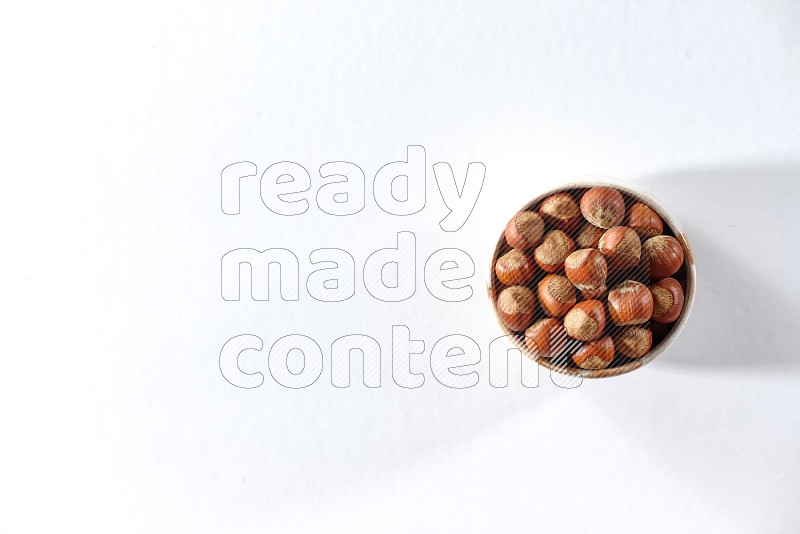 A beige ceramic bowl full of hazelnuts on a white background in different angles