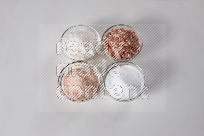 4 glass bowls filled with table salt, coarse sea salt, fine himalayan salt and coarse himalayan salt on white background