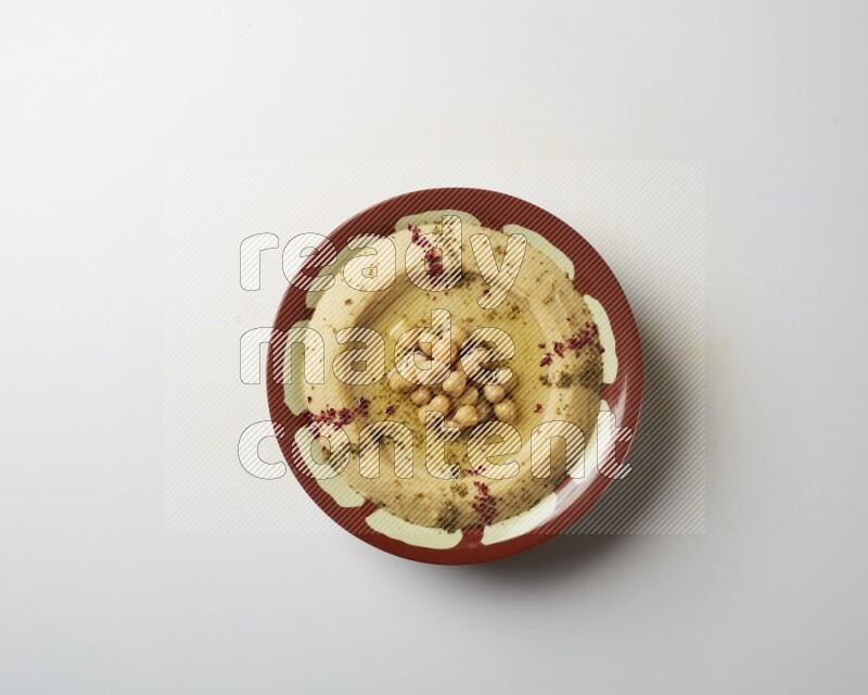 Hummus in a traditional plate garnished with zaatar & sumak on a white background