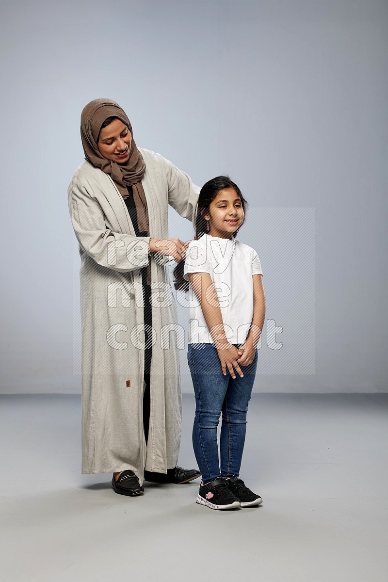 Mom standing styling hair for her daughter on gray background