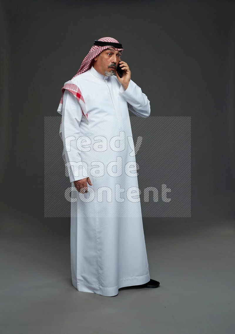 Saudi man with shomag Standing talking on phone on gray background