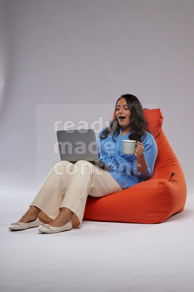 A woman sitting on an orange beanbag and working on laptop
