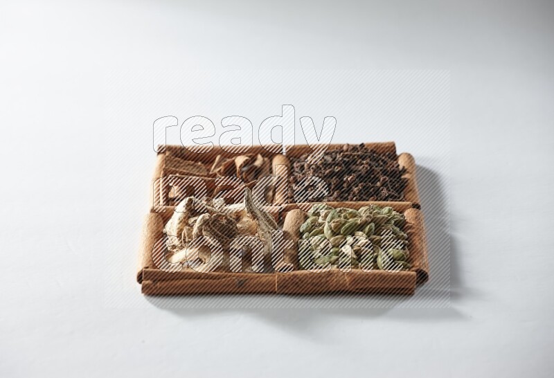 4 مربعات من أعواد القرفة ممتلئة بالهيل والقرفة والقرنفل والزنجبيل المجفف على أرضية بيضاء