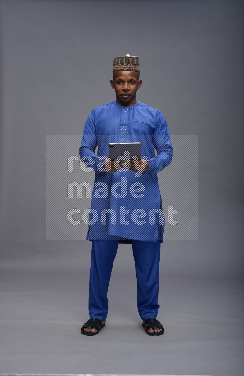 Man wearing Nigerian outfit standing working on tablet on gray background