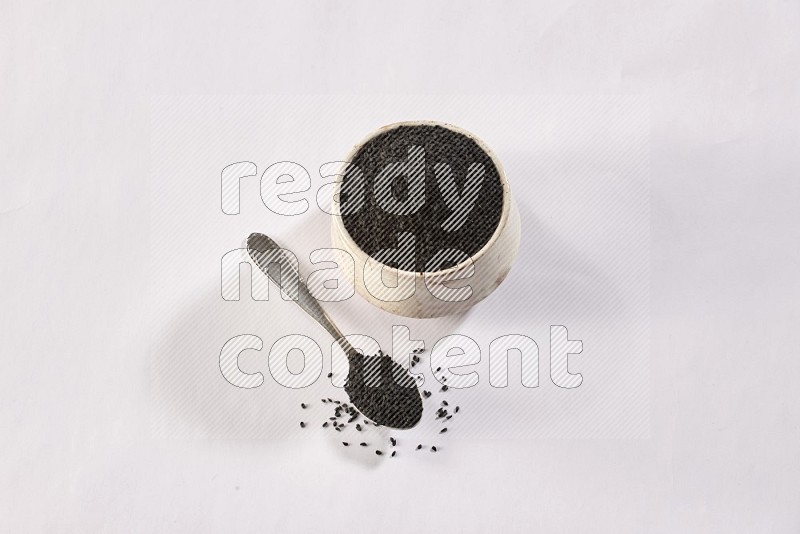 A beige pottery bowl and a metal spoon full of black seeds and more seeds spread on a white flooring in different angles