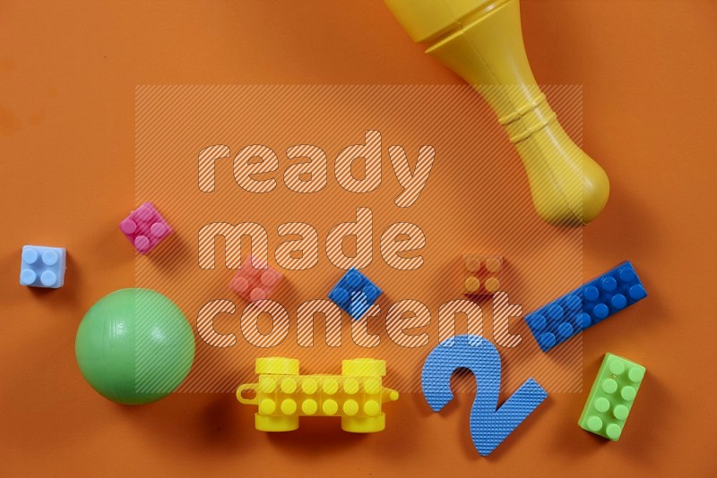 Plastic building blocks, balls and bowling pins on orange background in top view (kids toys)