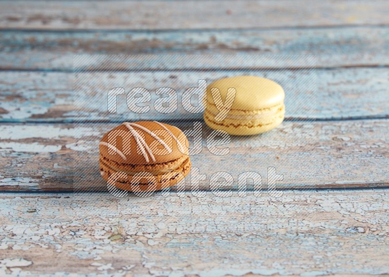 45º Shot of of two assorted Brown Irish Cream, and Yellow Vanilla macarons on light blue background
