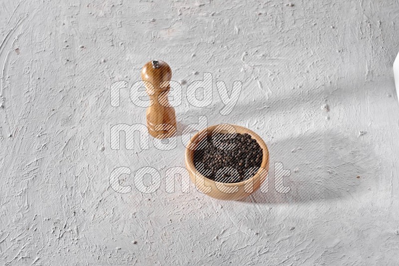 حبات الفلفل الأسود في وعاء خشبي مع مطحنة خشبية علي خلفية بيضاء