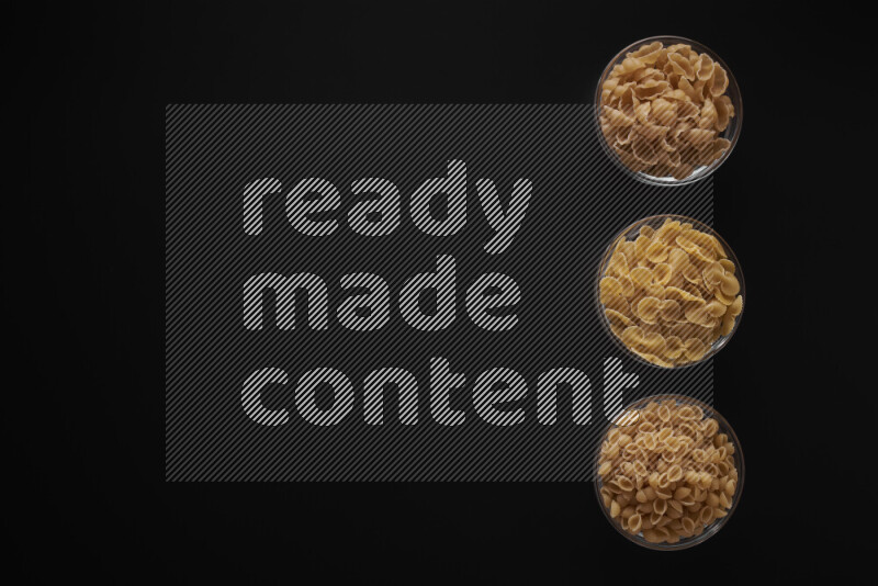 Different pasta types in 3 glass bowls on black background