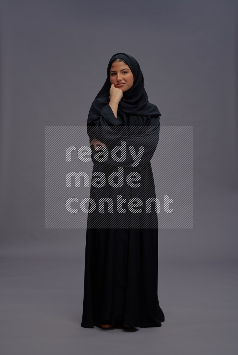 Saudi woman wearing Abaya standing interacting with the camera on gray background
