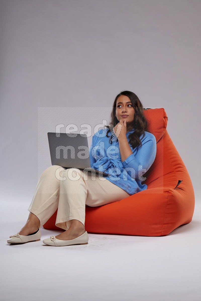 A woman sitting on an orange beanbag and working on laptop