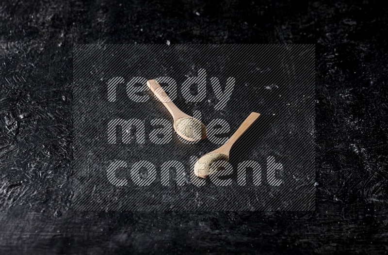 2 wooden spoons full of white pepper powder on textured black flooring