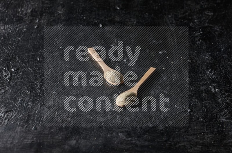2 wooden spoons full of white pepper powder on textured black flooring