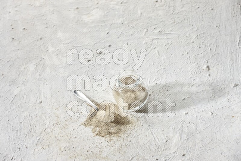 Herbal Glass jar full of white pepper powder and metal spoon full of powder on textured white flooring