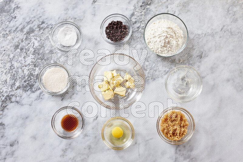 Cookies step by step with its ingredient, flour, butter, brown sugar, egg, vanilla extract, white sugar, chocolate chips and baking soda on grey marble background
