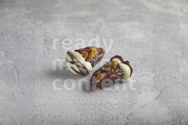 two pistachio stuffed dates covered with white chocolate with dark chocolate drizzle on a light grey background