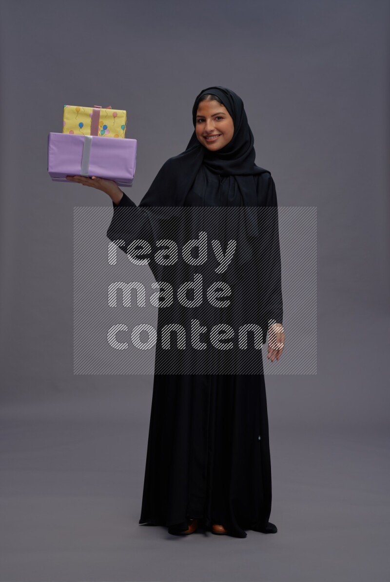 Saudi woman wearing Abaya standing holding gift box on gray background