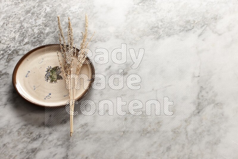 Wheat stalks on decorative pottery plate on grey marble background