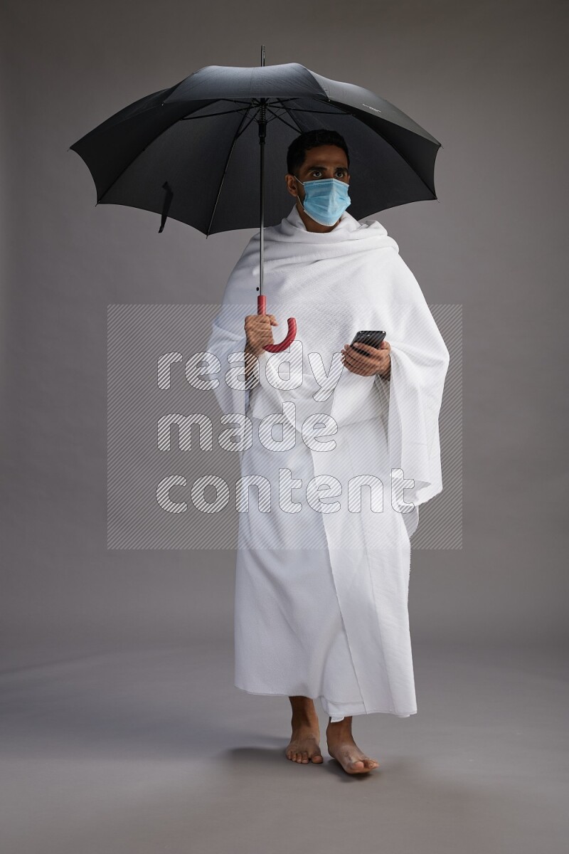 A man wearing Ehram and mask Standing holding umbrella on gray background on gray background