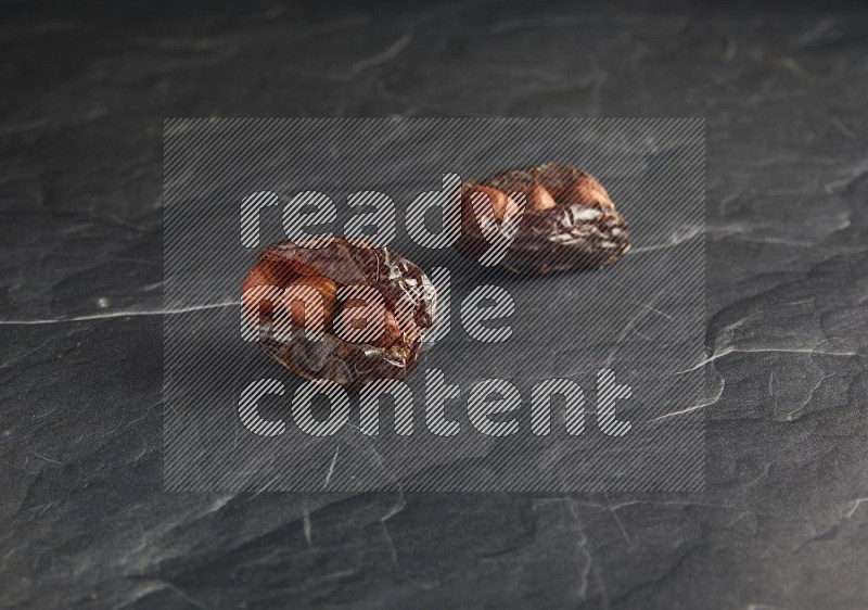 two hazelnuts stuffed madjoul dates on a black textured background