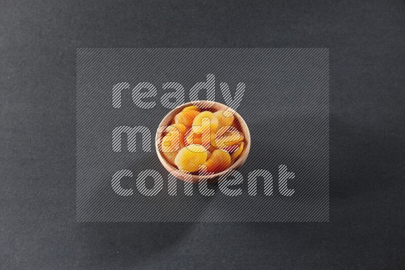 A wooden bowl full of dried apricots on a black background in different angles
