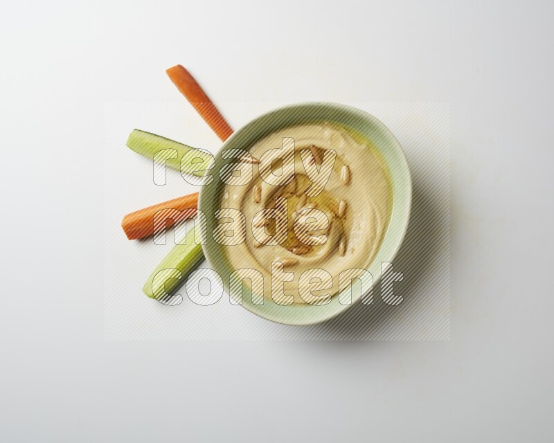 Hummus in a green plate garnished with pine nuts on a white background