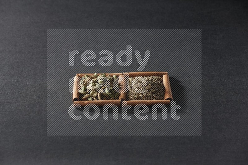 مربعان من أعواد القرفة ممتلئان بحبوب الكمون وحبوب الهيل علي خلفية سوداء