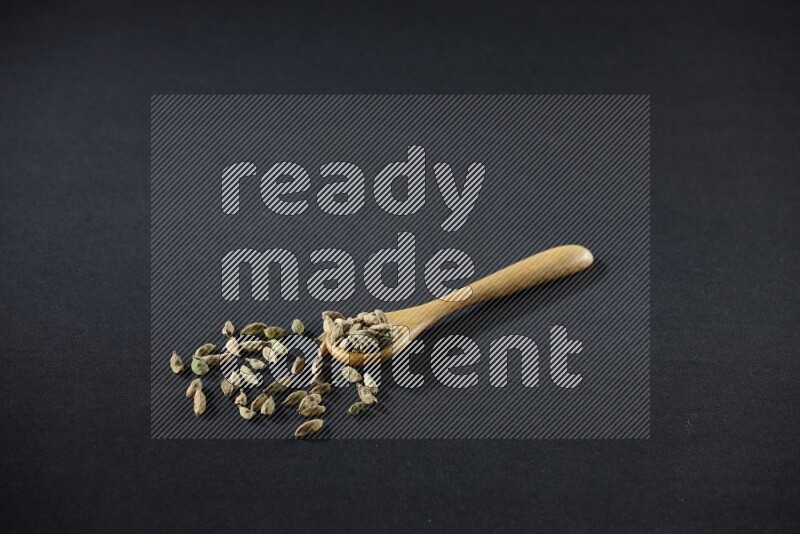 A wooden spoon full of cardamom on black flooring